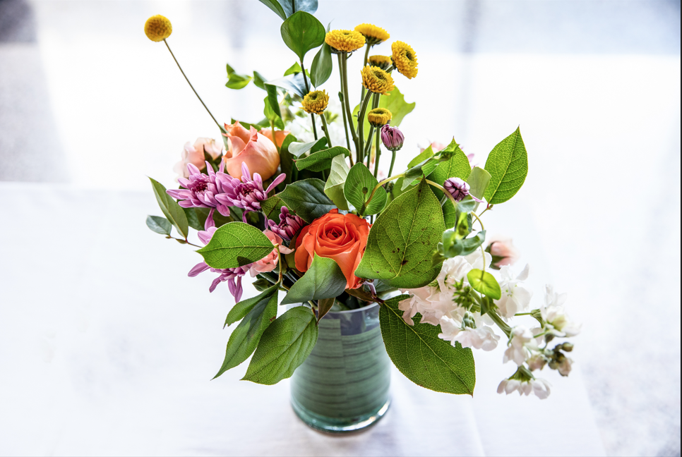 Orange roses, purple chrysanthemums, and yellow billy balls in a green ceramic vase