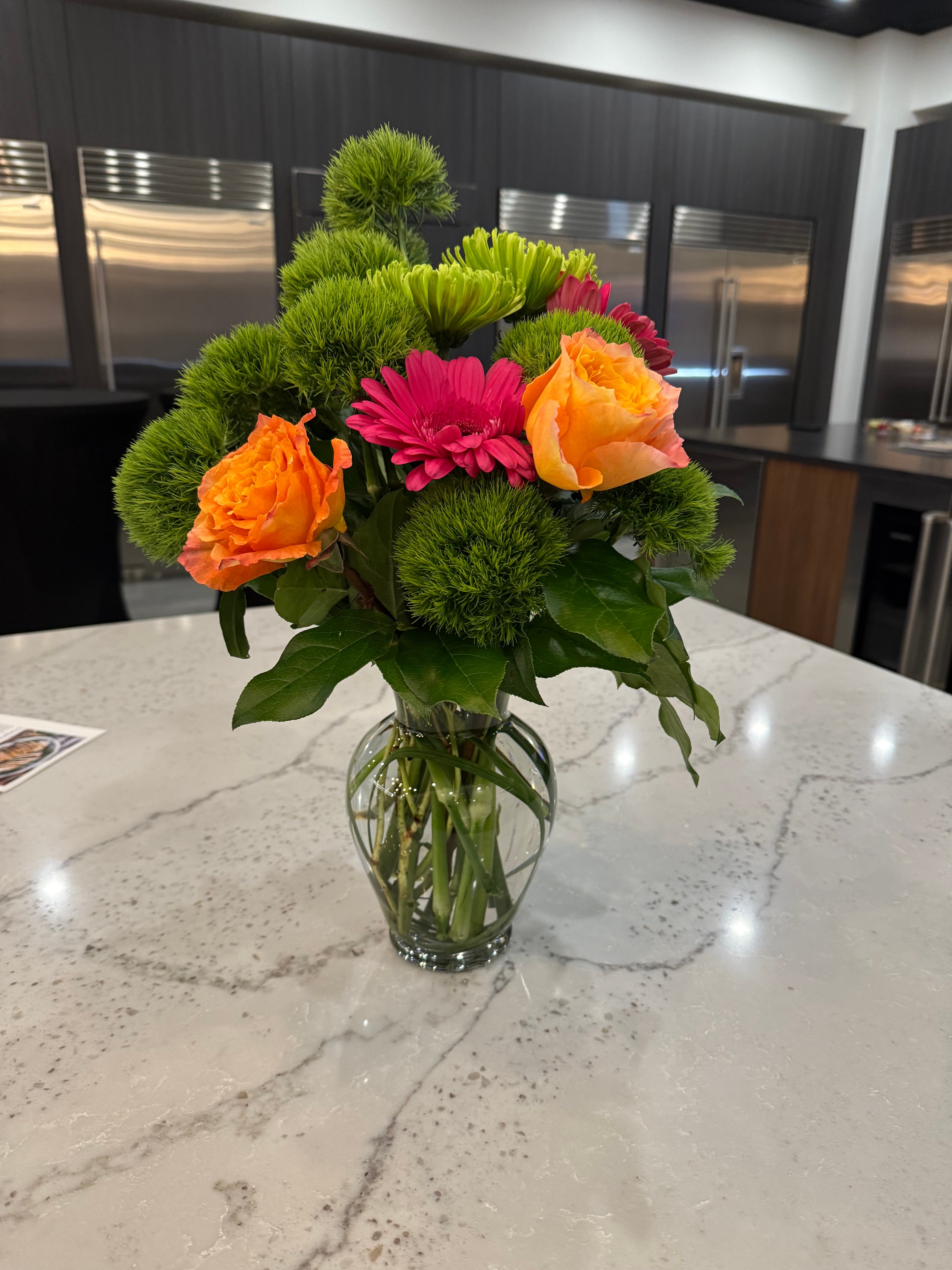 Orange roses and pink gerberas with green chrysanthemums in a glass vase on marble counter