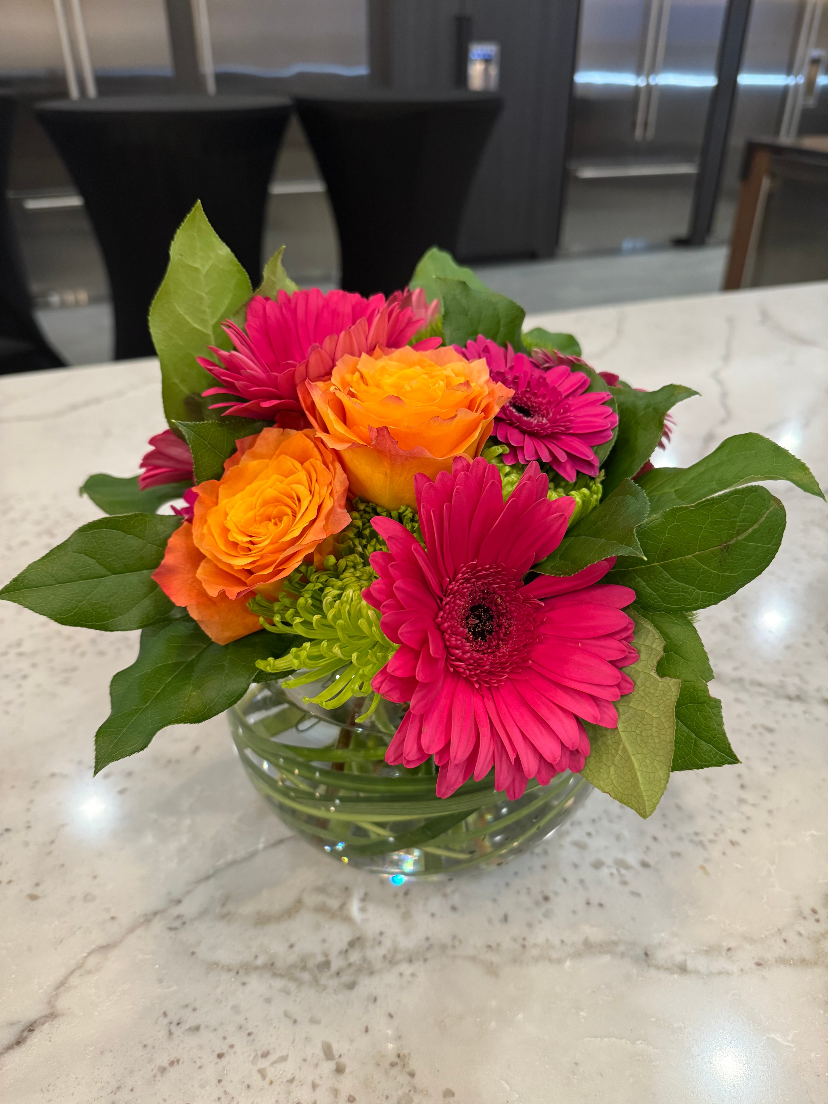 Hot pink gerberas and orange roses in a round glass fishbowl vase on marble counter