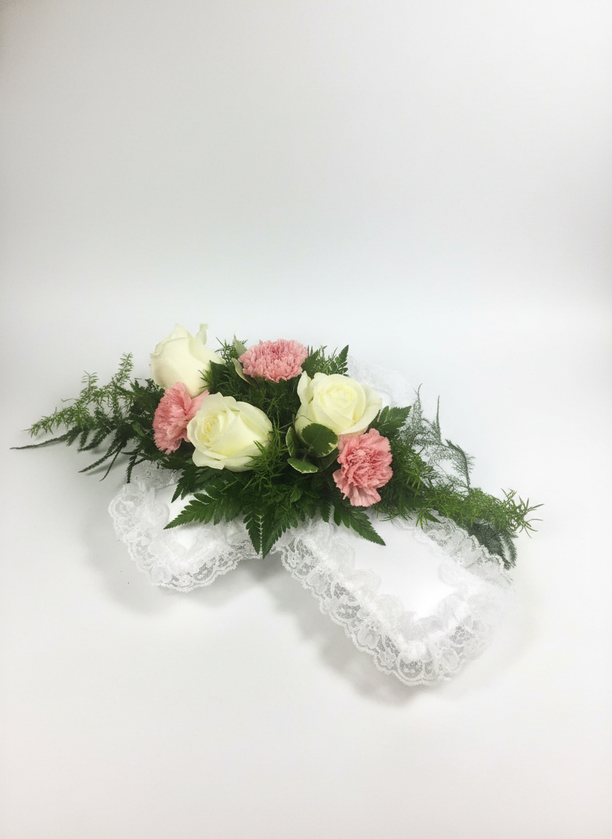 White roses and pink carnations on lace pillow with greenery