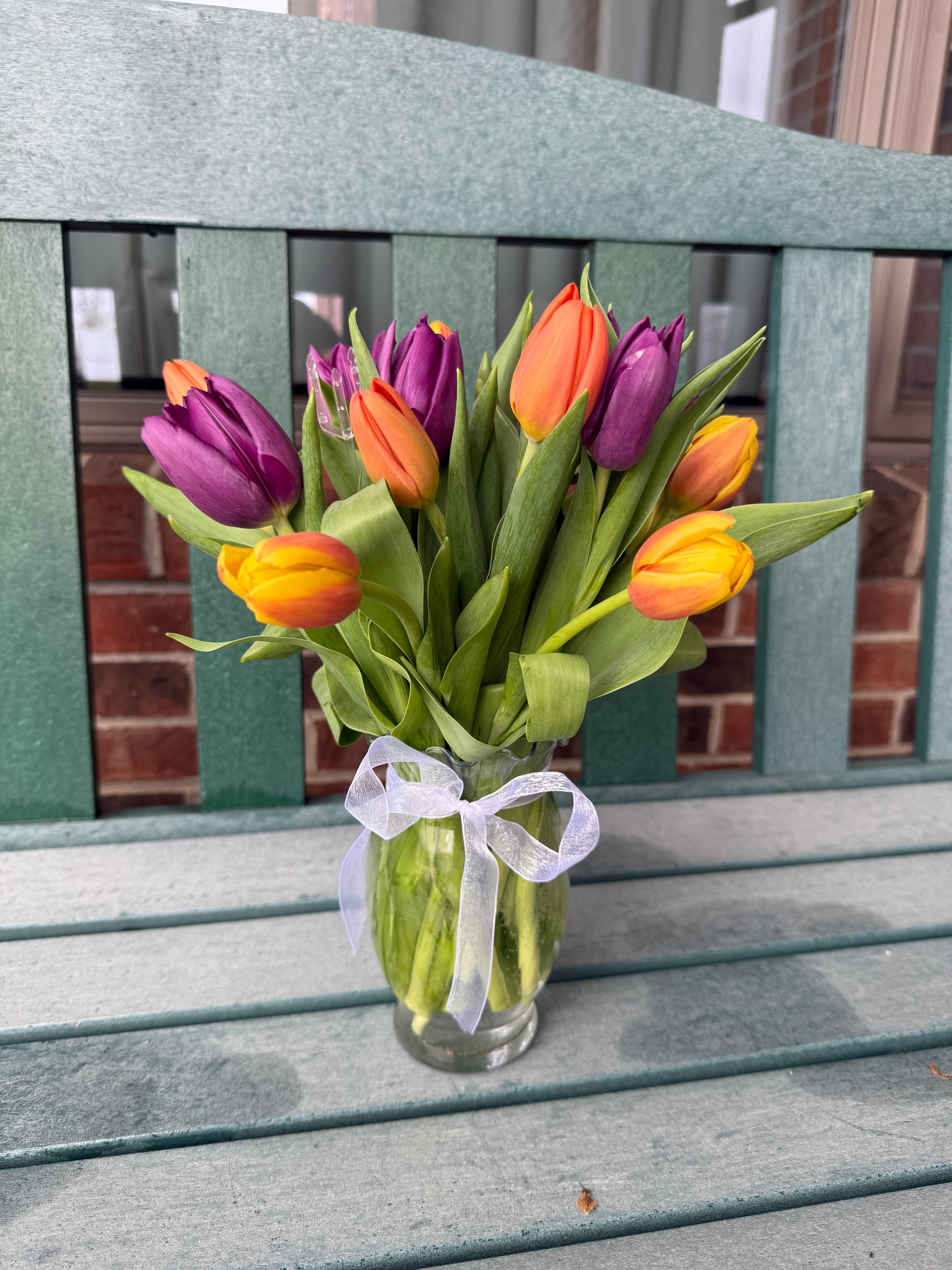 Colorful tulip bouquet in a glass vase with white ribbon