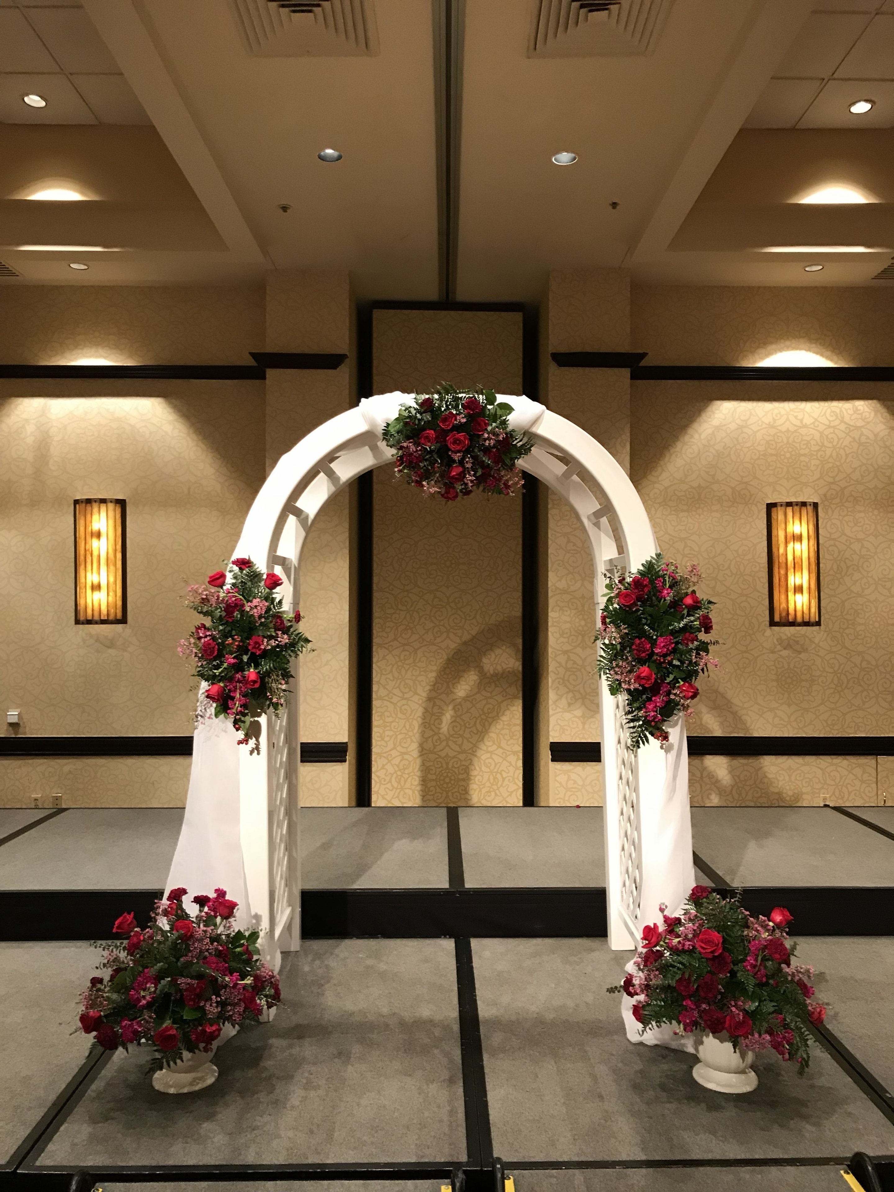 White arch with red rose floral arrangements in ballroom ceremony space
