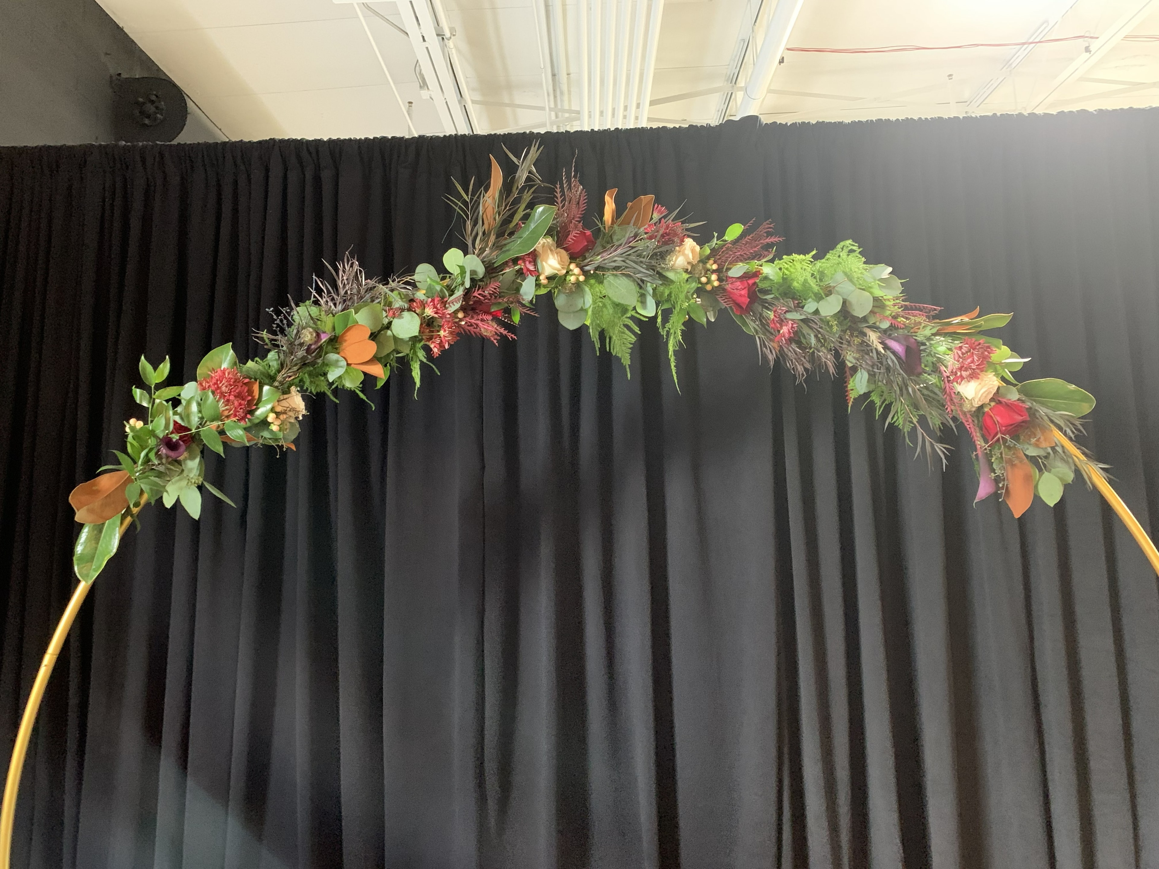 Autumn floral arch with burgundy, orange, and greenery on gold hoop frame