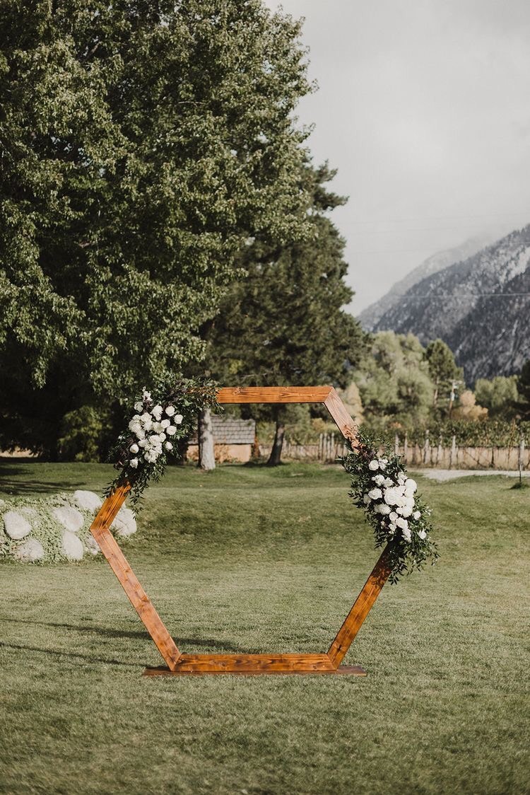 Wooden hexagonal wedding arch with white floral clusters in mountain valley
